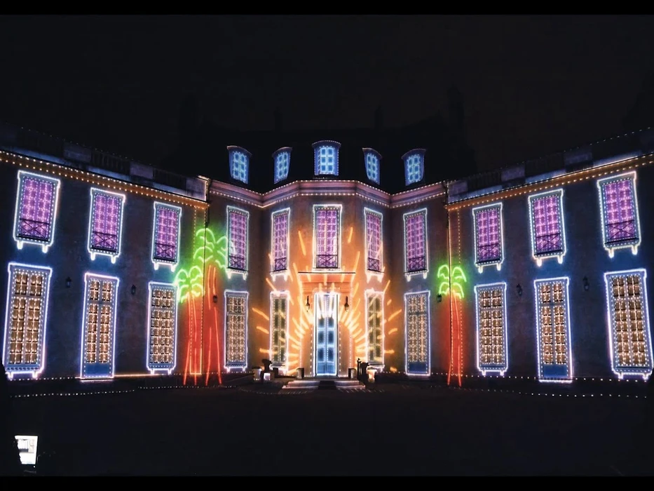 Façade illuminée d'un manoir classique de nuit, projection lumineuse colorée sur la pierre