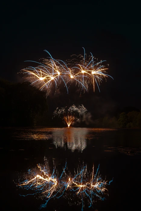 Feu d'artifice nocturne au-dessus d'un lac, reflets lumineux sur l'eau calme