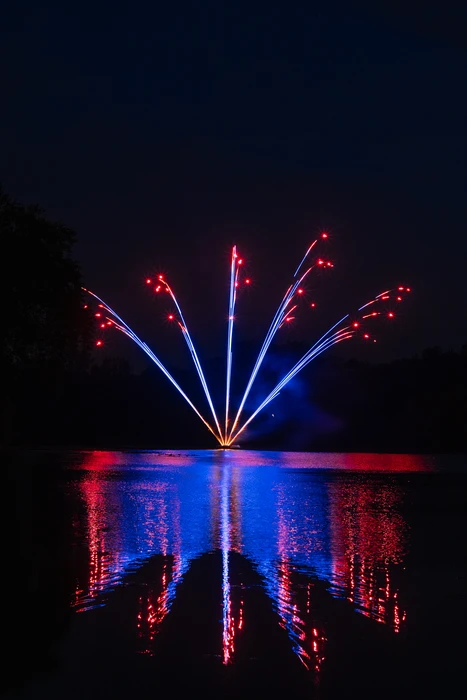 Feu d'artifice nocturne tiré depuis une surface d'eau, avec reflets colorés