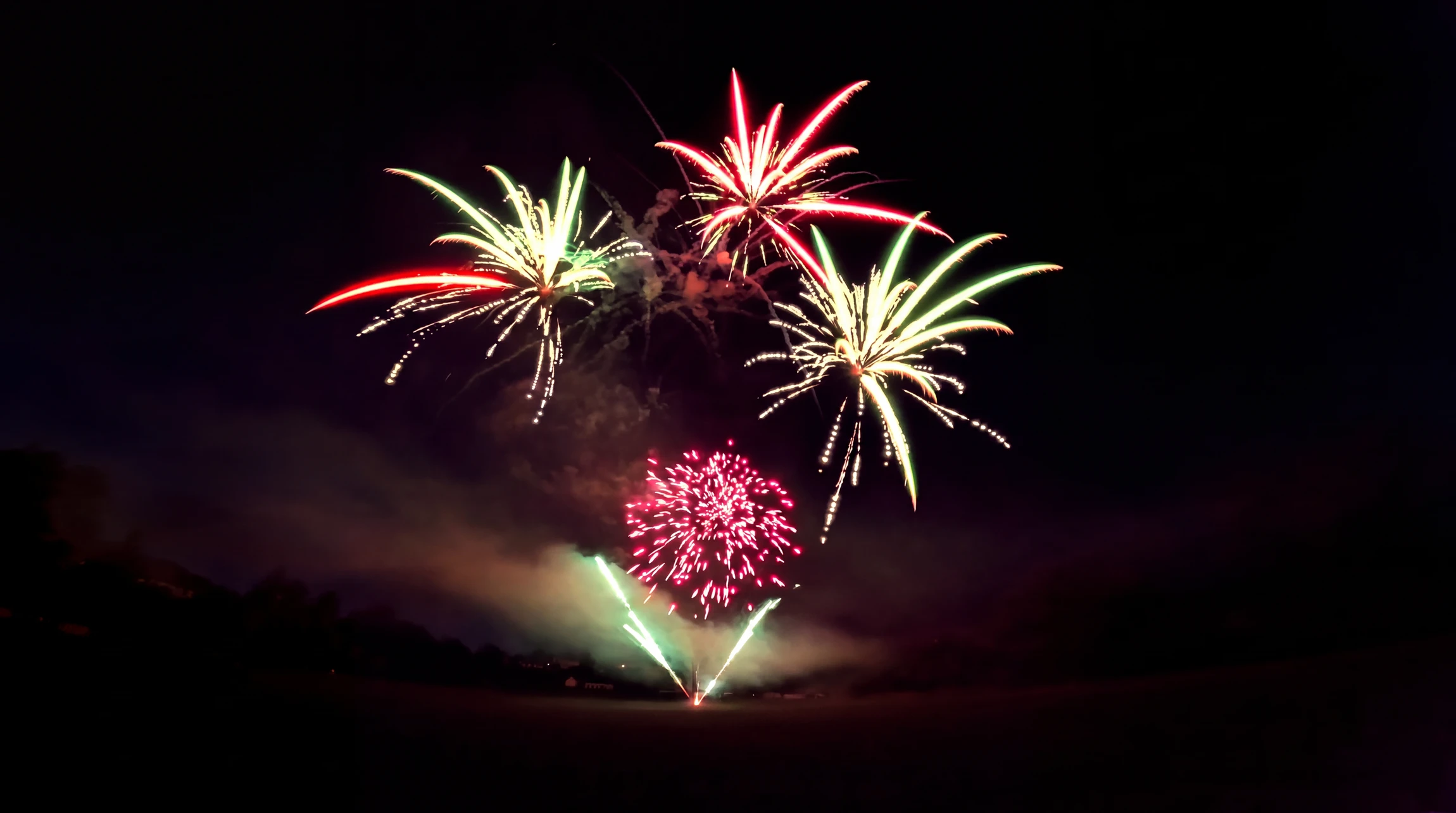 Spectacle pyrotechnique nocturne, plusieurs explosions simultanées de feux d'artifice aux couleurs vives : rouge, vert et rose