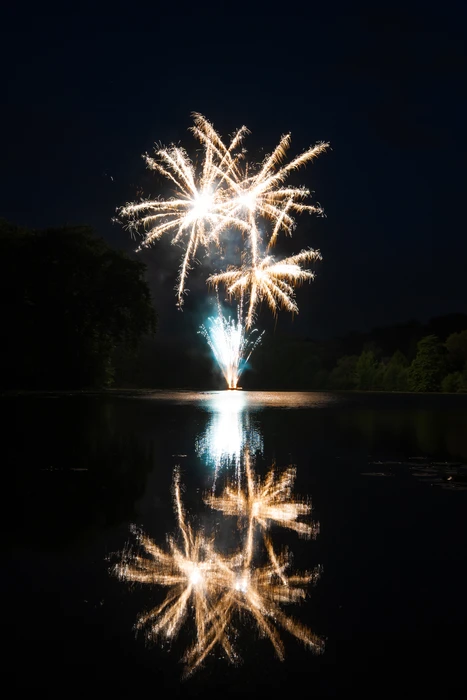 Feu d'artifice nocturne tiré depuis un lac, avec reflet parfait sur l'eau calme