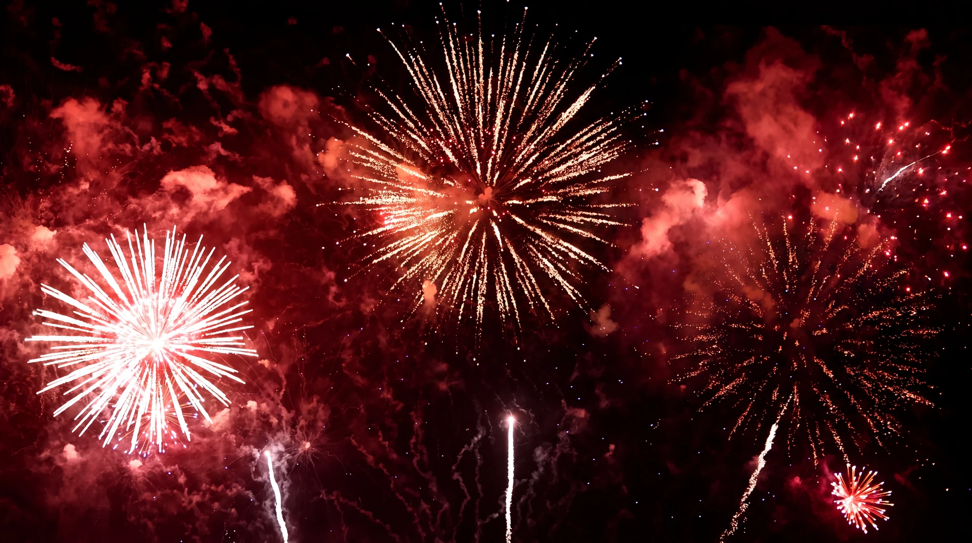 Spectacle pyrotechnique nocturne, plusieurs explosions simultanées de feux d'artifice aux couleurs vives : rouge, vert et rose